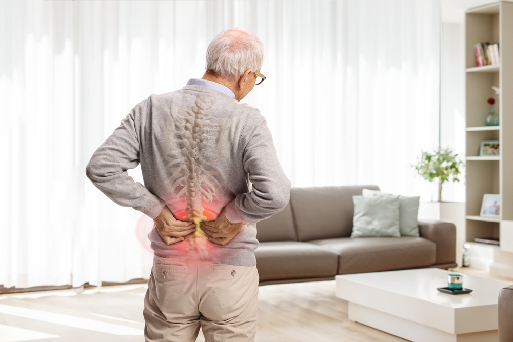 Older man holding lower back in pain, an early symptom of ankylosing spondylitis.